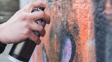 Mano con una lata de aerosol dibujando graffiti en una pared.