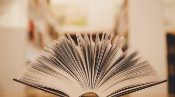 Libro abierto en un escritorio y en medio de dos estanterías.