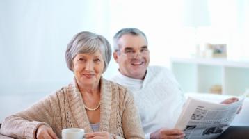 Pareja de adultos mayores tomando café y leyendo el periódico.