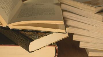 Libros apilados de manera desordenada y el primer libro abierto por la mitad. 