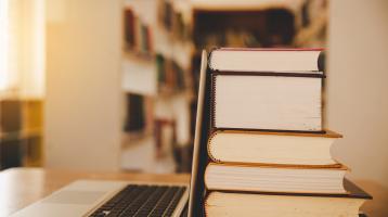 Computadora personal junto a diversos libros apilados en una torre. 