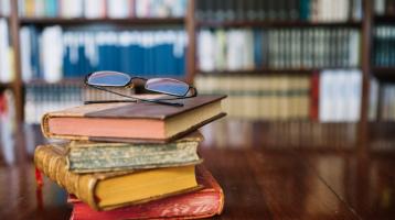 Libros apilados verticalmente y encima unos anteojos.