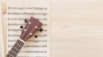 Vista superior de mastil de una guitarra sobre una partitura. 