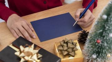 Manos tomando un lapicero sobre una hoja azul en una mesa de madera con adornos navideños. 