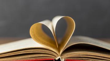 Fondo gris, Sobre una mesa un libro abierto, con sus páginas en forma de corazón. 