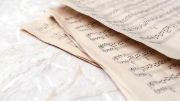 Fondo blanco. A la derecha varias partituras musicales. 