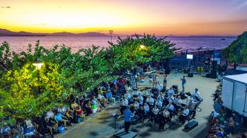 Hermosa fotografía de la Banda de Conciertos de Puntarenas tocando en el Faro y con perspectiva aérea donde se aprecia el mar del puerto detrás de ellos