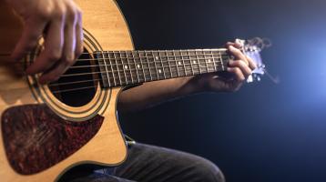En primer plano, persona tocando guitarra acústica.