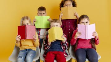 Fondo amarillo. Niños cubriendo sus caras con libros. 