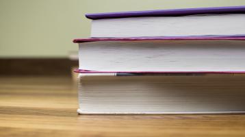 Fondo blanco, sobre mesa de una madera, tres libros apilados a la derecha.