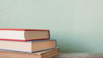 Fondo verde claro. Sobre mesa de madera, a la izquierda tres libros apilados horizontalmente,