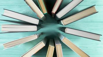 Sobre mesa de madera color celeste, desde vista superior libros uniendo sus lomos para formar un círculo.