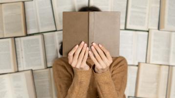 Fondo de libros abiertos. Persona sosteniendo el libro tapando su cara. 