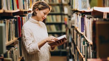 Mujer en una biblioteca sosteniendo un libro. 