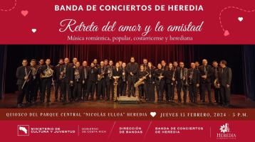 Foto de la Banda de Conciertos de Heredia sobre un escenario con fondo rojo y letras blancas rodeadas de corazones