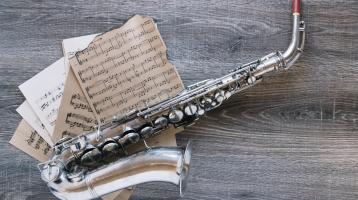 Fondo de madera. Un saxofón sobre partituras musicales. 
