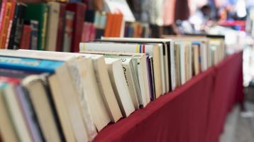 Sobre una mesa con mantel rojo, libros ordenados horizontalmente.