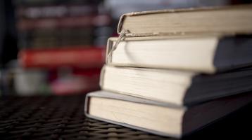 Fondo difuminado. Sobre una mesa, una torre de libros a la derecha.