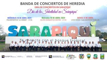 Músicos de la Banda de Heredia sentados en fila bajo las letras gigantes que dicen Sarapiquí