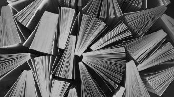 En tonos grises varios libros juntos entreabiertos vistos desde arriba