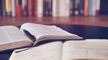 Un estante con libros de fondo y 2 libros abiertos