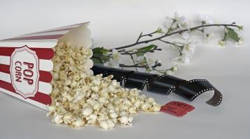 Unas palomitas regadas junto a una cinta de película, un ticket y unas flores