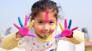 Una niña con la cara y manos pintadas con pintura de colores