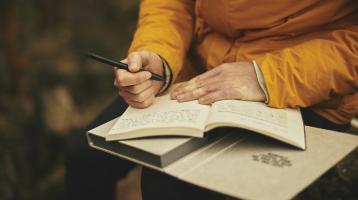 Parte de una persona con un libro abierto y una pluma en la mano