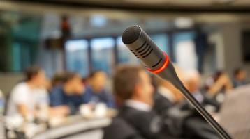 Un micrófono y el fondo desenfocado con varias personas en un tipo auditorio