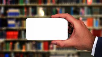 Una persona sosteniendo un celular y de fondo una biblioteca